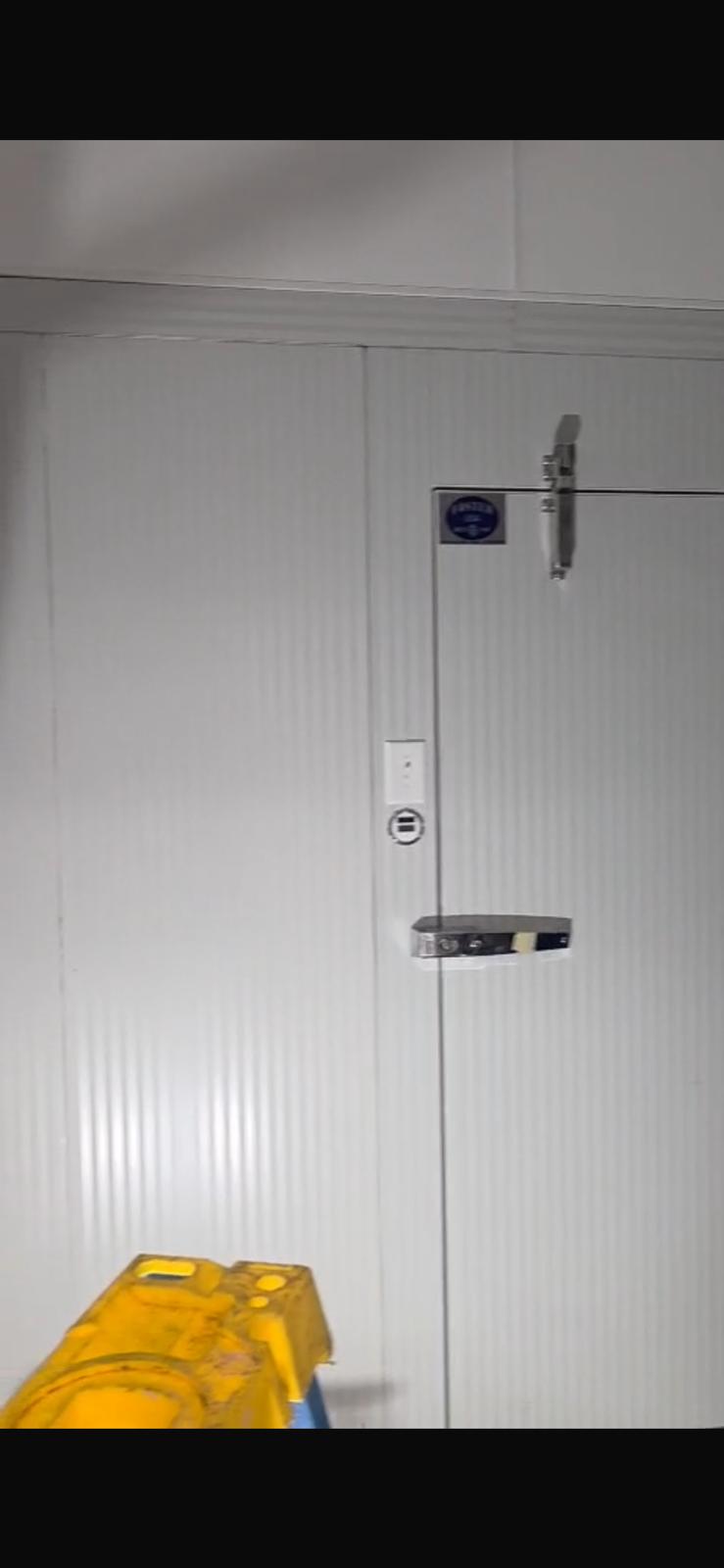 A Foster USA walk-in cooler door in service, showing the corrugated panel finish, cam-lock latch, and Foster USA nameplate