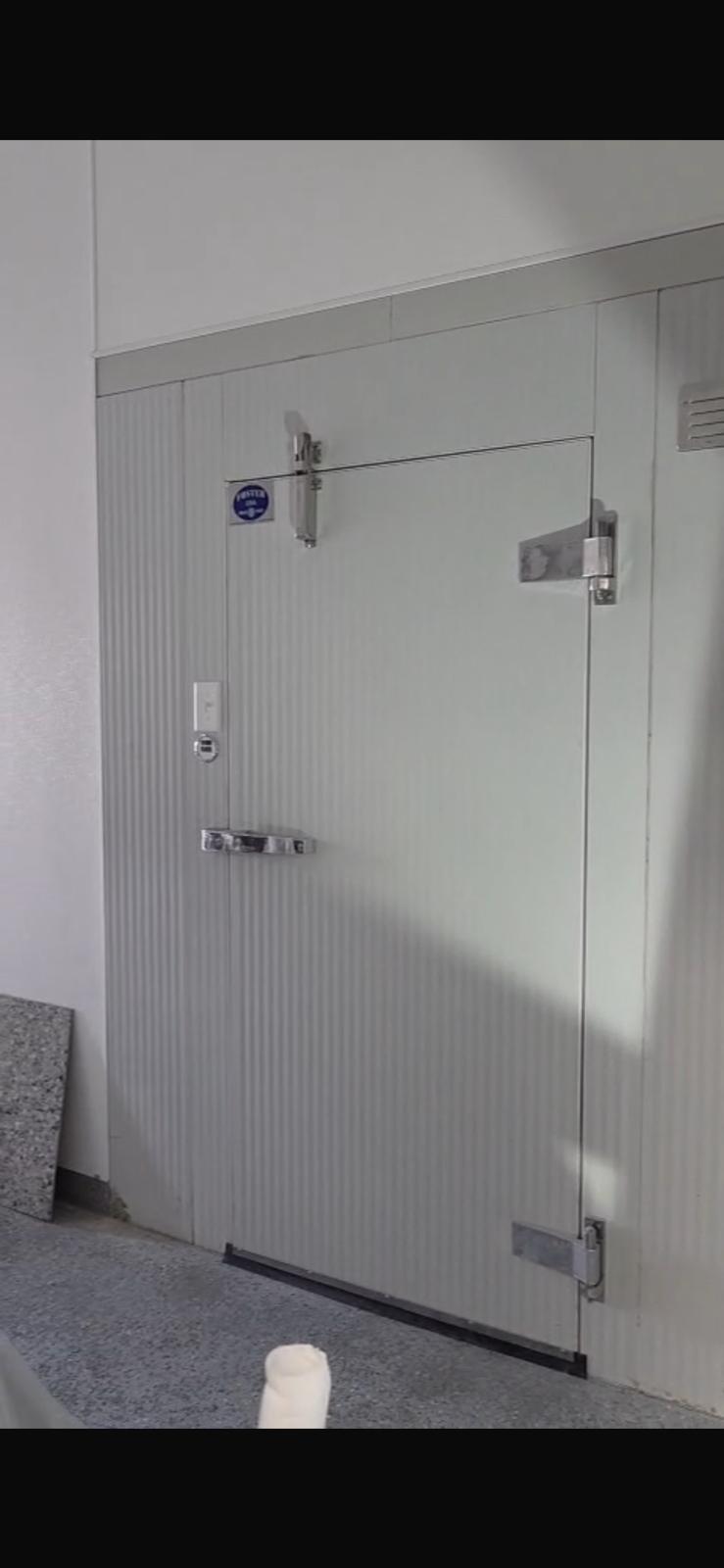 Close-up of a Foster USA walk-in cooler door showing the corrugated panel, cam-lock latch, and blue Foster USA nameplate